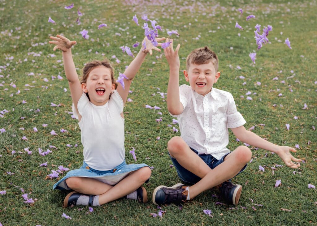 Little brother and sister throwing Jacaranda flowers in the air