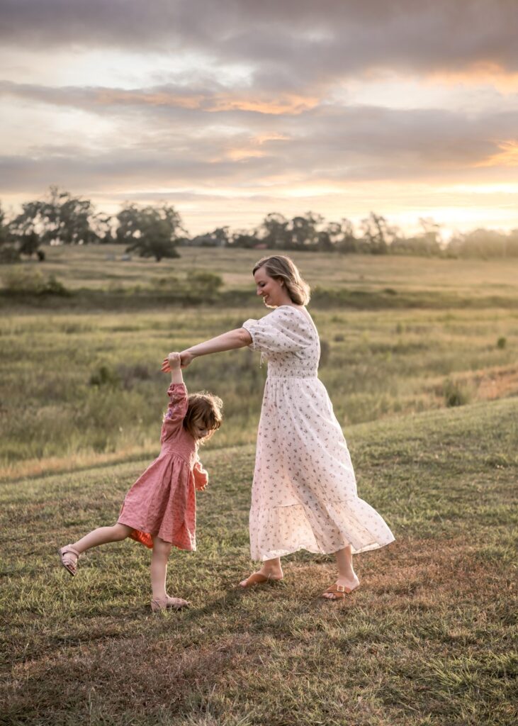 mother and daughter dancing in a field at sunset near Ipswich