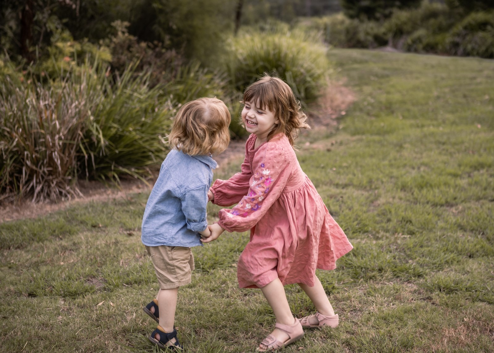 Little brother and sister dancing and playing together in the park in Ipswich