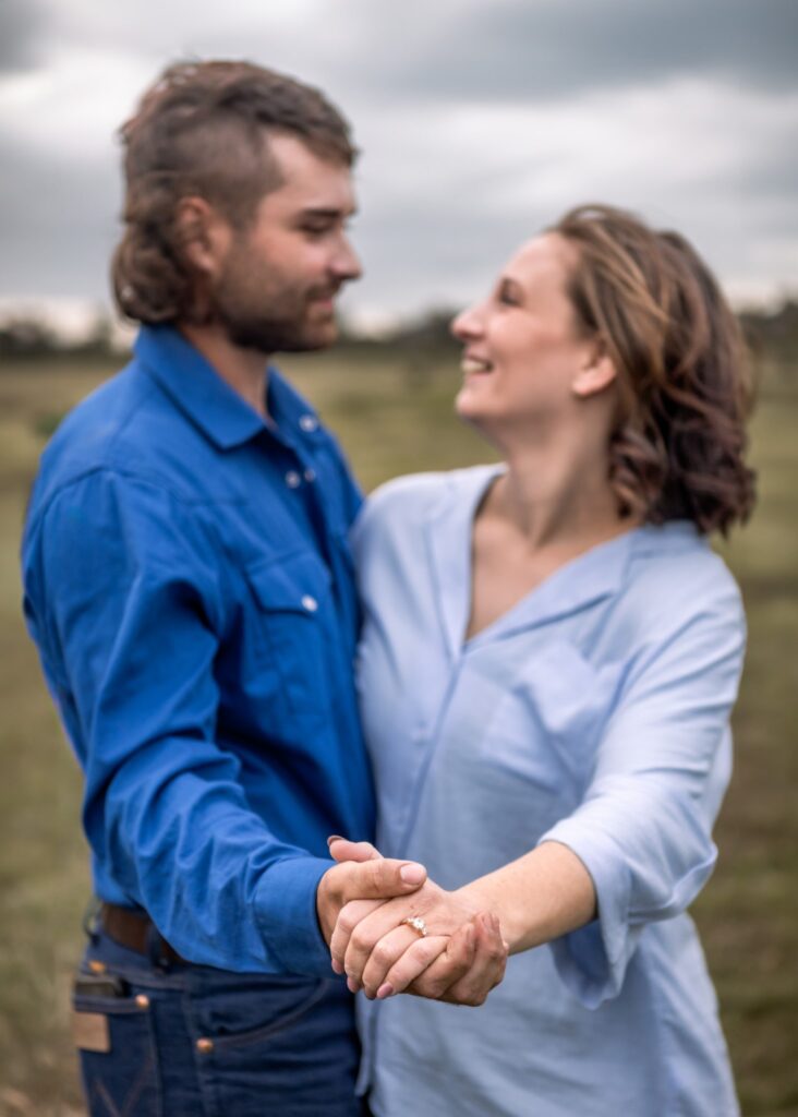 Couple in a field holding hands, smiling at each other, showcasing outdoor photography in Ipswich.